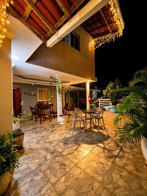 An outdoor patio area with tiled flooring, wooden furniture, and potted plants. - Pousada Raízes do Porto (Ipojuca)