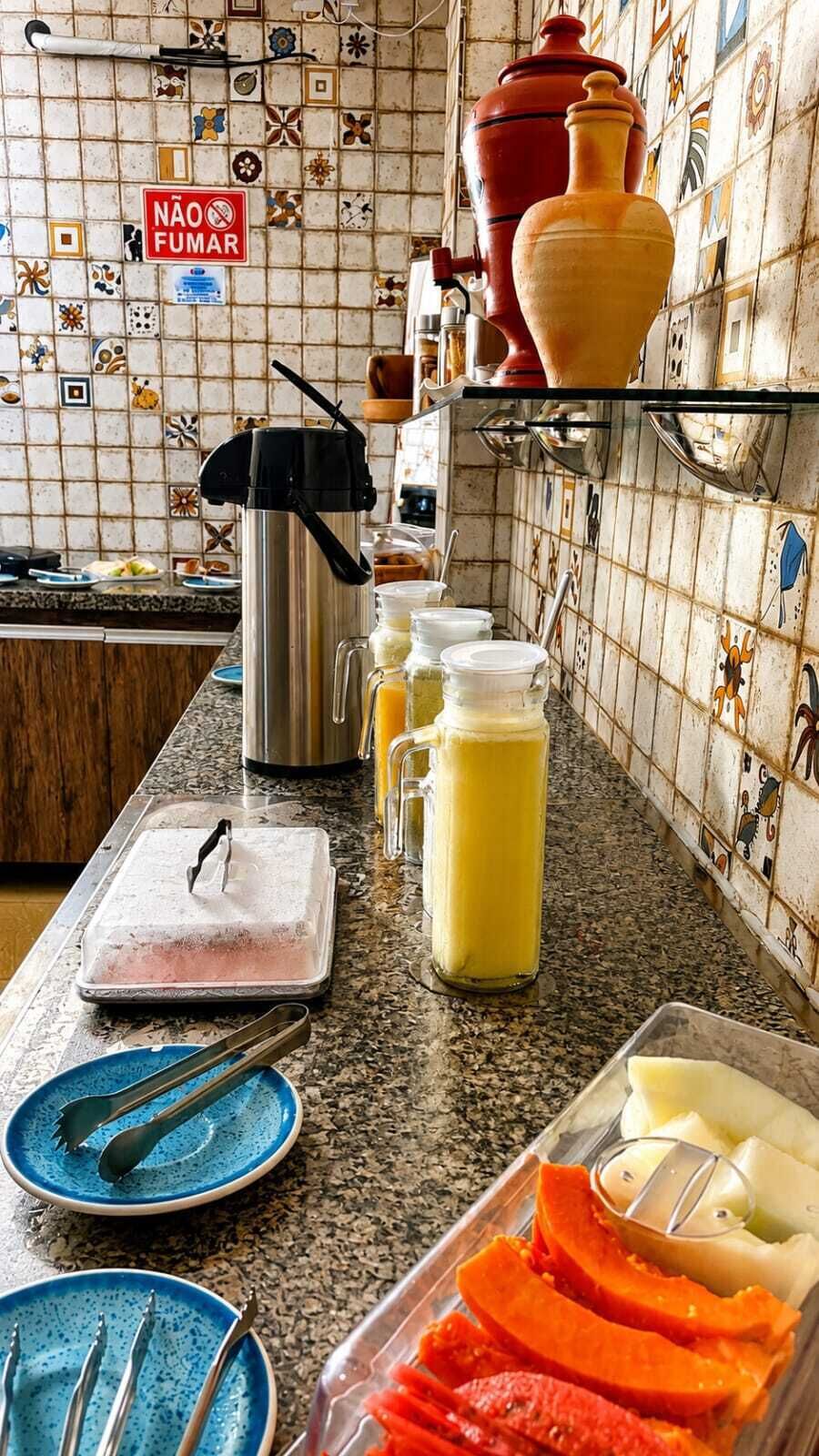Eine Küche mit gefliestem Spritzschutz, einer Kaffeemaschine, einem Thermosbehälter und Lebensmitteln auf der Arbeitsfläche.