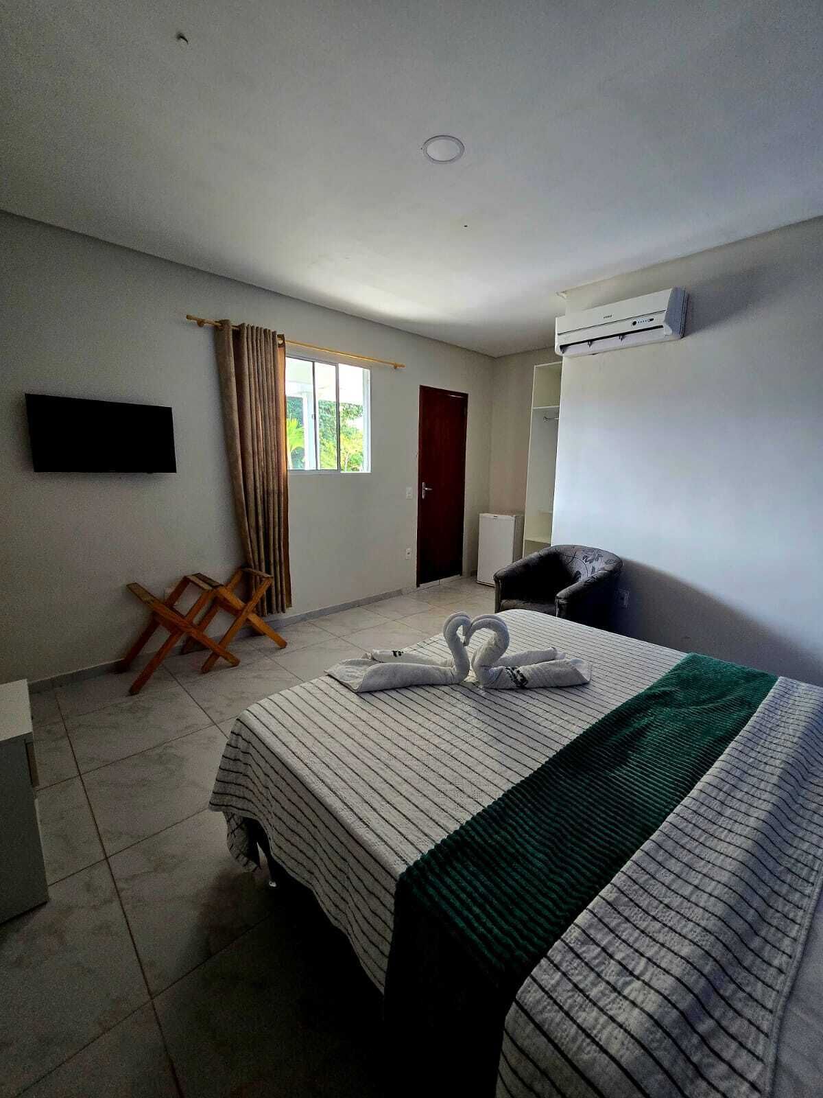 Una habitación de hotel con cama, televisor, ventana con cortinas, puerta y aire acondicionado.