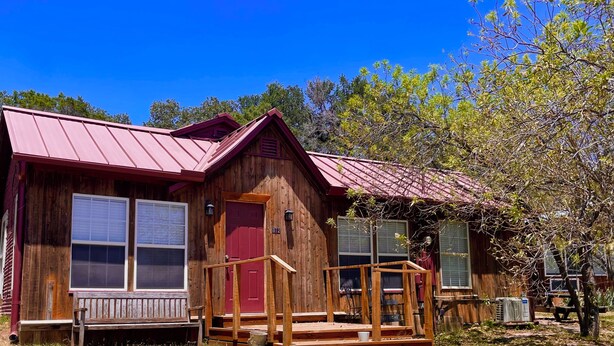 Une cabane rustique avec une porte rouge, une véranda avec des marches et un toit en métal.