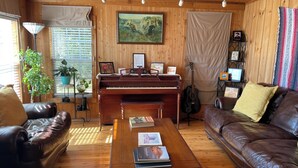 Un salon chaleureux avec un piano en bois, des canapés en cuir, une table basse avec des livres, une guitare et un tableau accroché au mur.