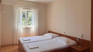 A simple, clean room with two single beds, a window with curtains, a bedside table, and a wall socket.
