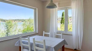 A room with a table and chairs, large windows with a view of a lake and trees, and a hanging light fixture.