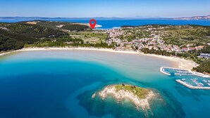 An aerial view of a coastal town with a beach, clear blue waters, and a marina.