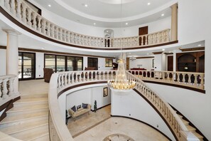 A grand interior with a central staircase, multiple balconies, and a chandelier.