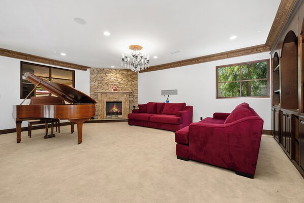 A spacious living room with a grand piano, a red sofa, and a fireplace.