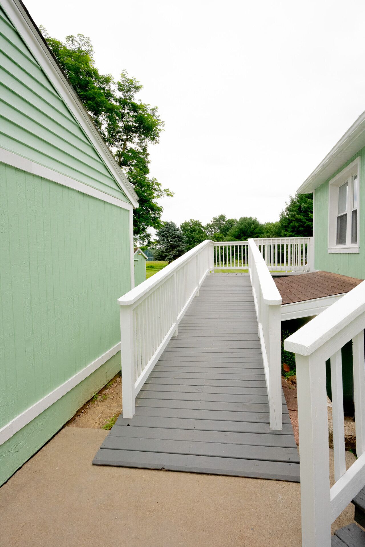 A wooden deck leading to a green building with white railings.