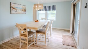Un coin repas avec une table et des chaises en bois, un luminaire suspendu et une fenêtre avec des rideaux.