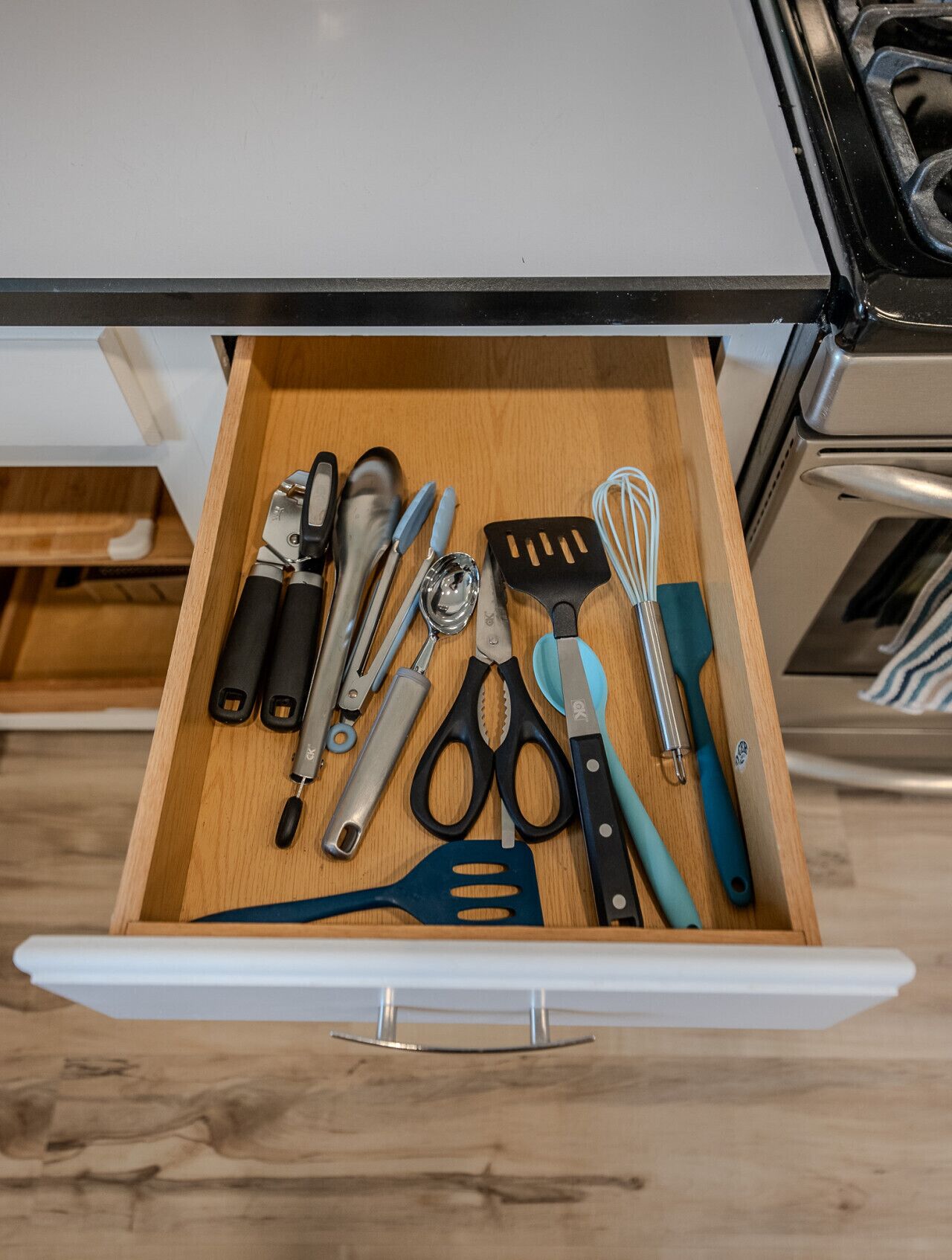 A kitchen drawer with various utensils including a spatula, whisk, and scissors.