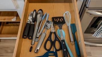 A kitchen drawer with various utensils including a spatula, whisk, and scissors.