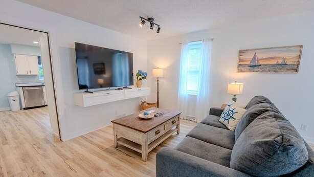 Un salon moderne avec un téléviseur à écran plat, une table basse en bois, un canapé gris et un tableau représentant des voiliers accroché au mur.