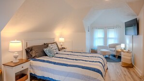 Une chambre à coucher avec un lit, des tables de chevet, une chaise, un téléviseur et une fenêtre avec des rideaux.