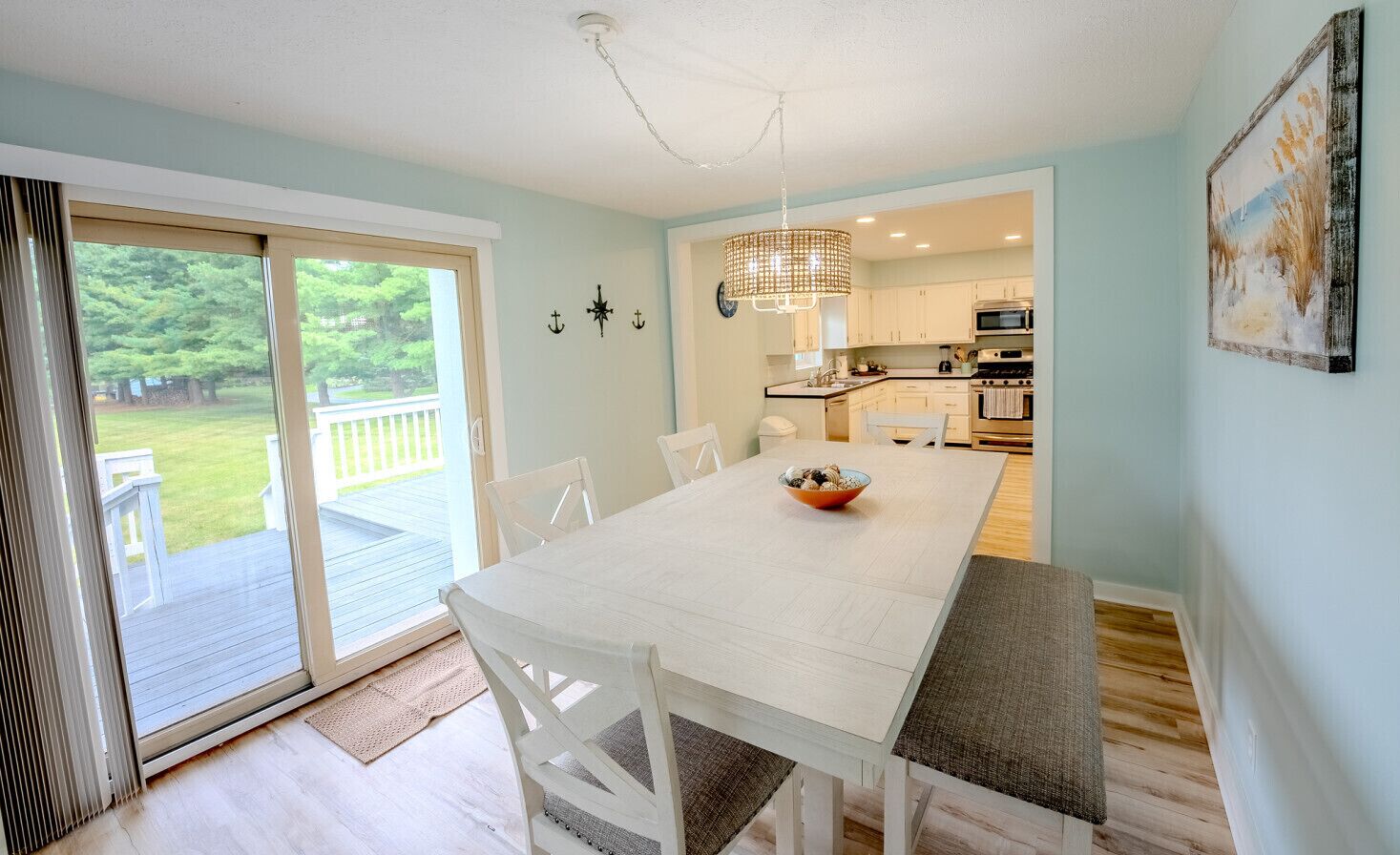 A dining area with a white table and chairs, a bench, a chandelier, and a view of the outdoors through a sliding glass door.