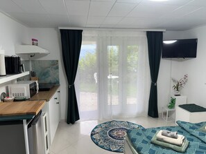 A compact living space with a kitchenette, a flat-screen TV, a dining area, and a view through the glass door. - Romantic studio surrounded by vineyards II (Laufen-Uhwiesen)