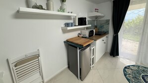 A modern kitchen with white cabinets, a microwave, and a coffee maker on the countertop. There are three vases with purple flowers on a shelf above the counter.