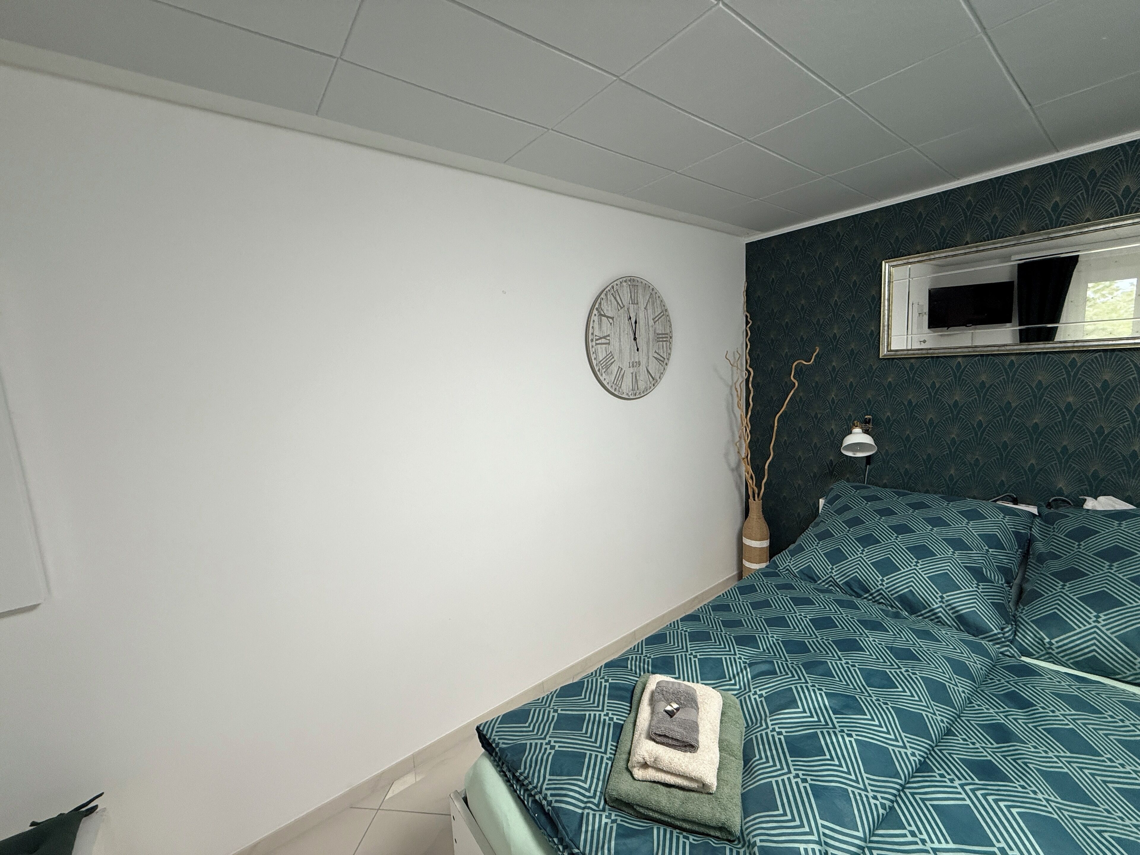 Ein Schlafzimmer mit einem Bett, einer Wanduhr, einem Spiegel und einem Fenster.