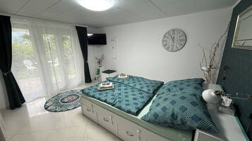 Ein Schlafzimmer mit einem Bett, einem Fernseher, einer Uhr und einem Fenster mit Vorhängen.