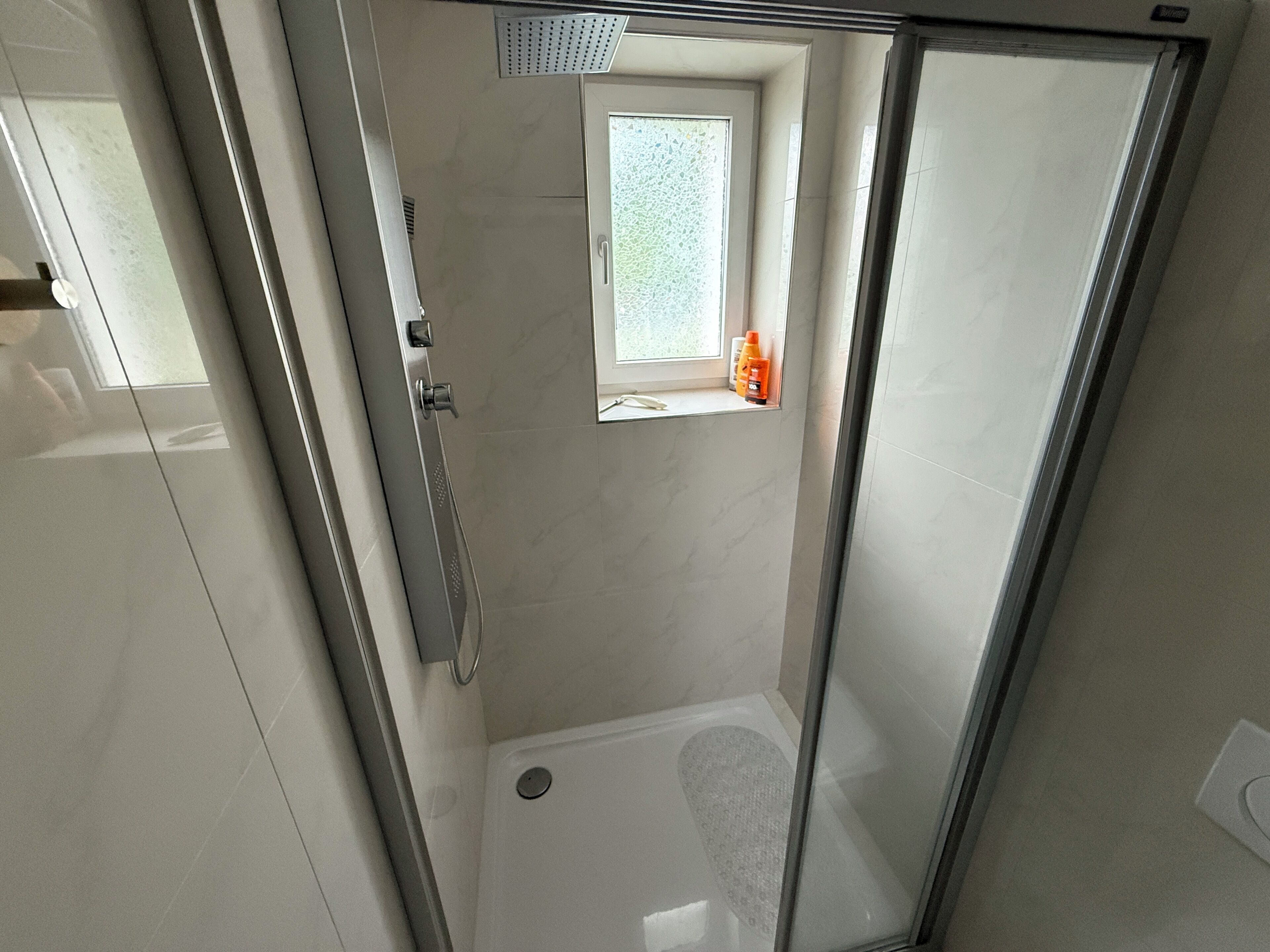A modern bathroom with a glass shower enclosure, a small window, and a toilet.