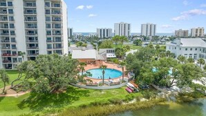 A high-rise building with multiple balconies, a swimming pool surrounded by trees, and a view of the ocean.