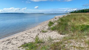 Ein Strand mit klarem Wasser, sandigem Ufer und einer Grünfläche.