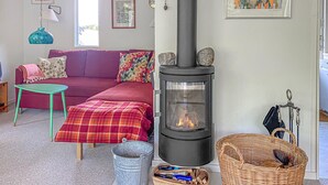 Ein gemütliches Wohnzimmer mit einer Couch, einem kleinen Tisch, einem Kamin und einem Korbwannenstuhl.