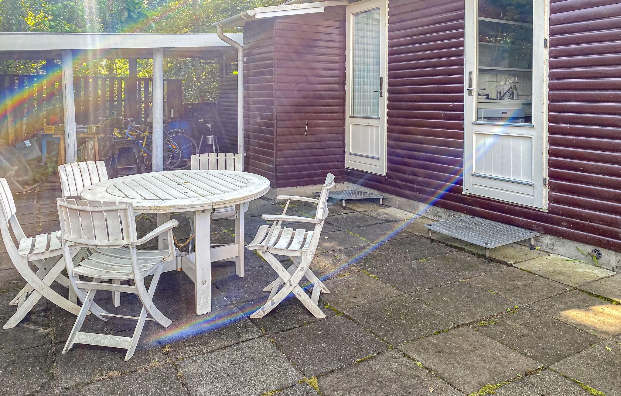 Eine Terrasse mit rundem Tisch und vier Stühlen, ein Holzboden und ein Haus mit violetter Fassade.