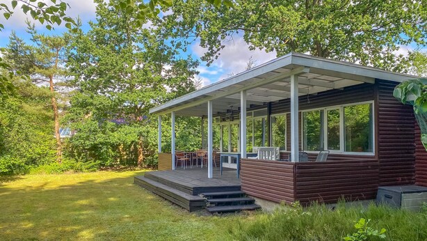 Eine Holzhütte mit einer überdachten Veranda, Sitzgelegenheiten im Freien und Blick auf den umliegenden Wald.