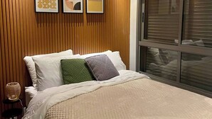 Un dormitorio moderno con un panel de madera en la pared, una cama grande con ropa blanca, y tres obras de arte enmarcadas sobre la cama.