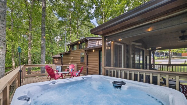 Un jacuzzi en una terraza con sillas, una cabaña de madera y vista a árboles.