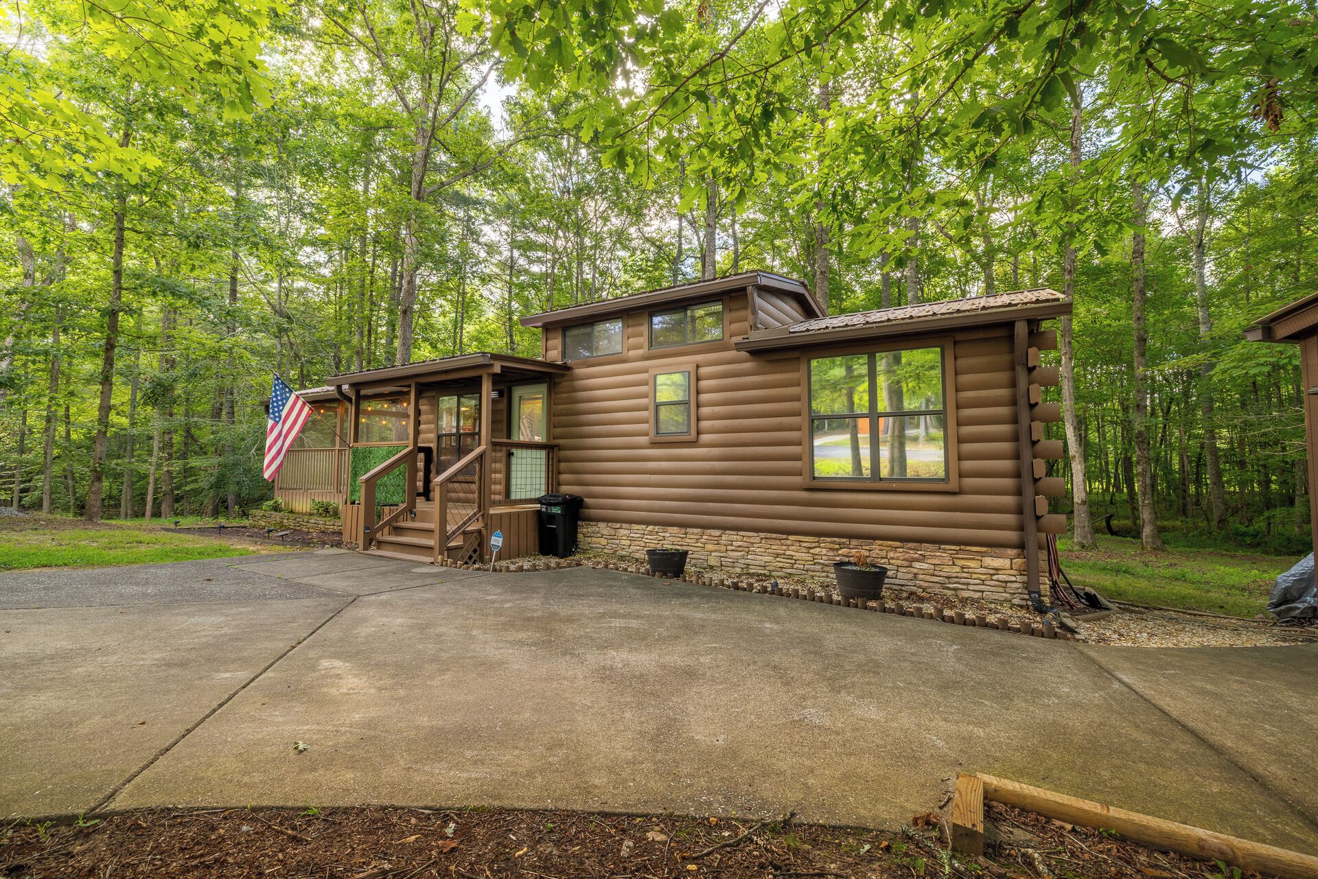 A log cabin with a porch, a flag, and a stone foundation.