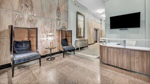 Un hall d’hôtel aux murs de marbre, avec deux espaces de détente dotés de fauteuils confortables, un comptoir de réception et un téléviseur fixé au mur.