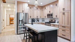 A modern kitchen with stainless steel appliances, wooden cabinets, and a central island with stools. - Scenic Location: Beautiful Townhome, 5 min to Base, Private Hot Tub, Walk to restaurants! (Park City)