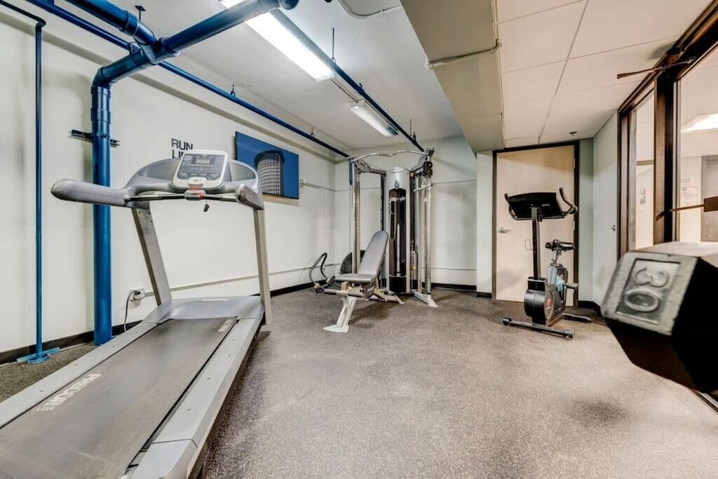 Un gimnasio con caminadora, máquinas de pesas y bicicleta estática.