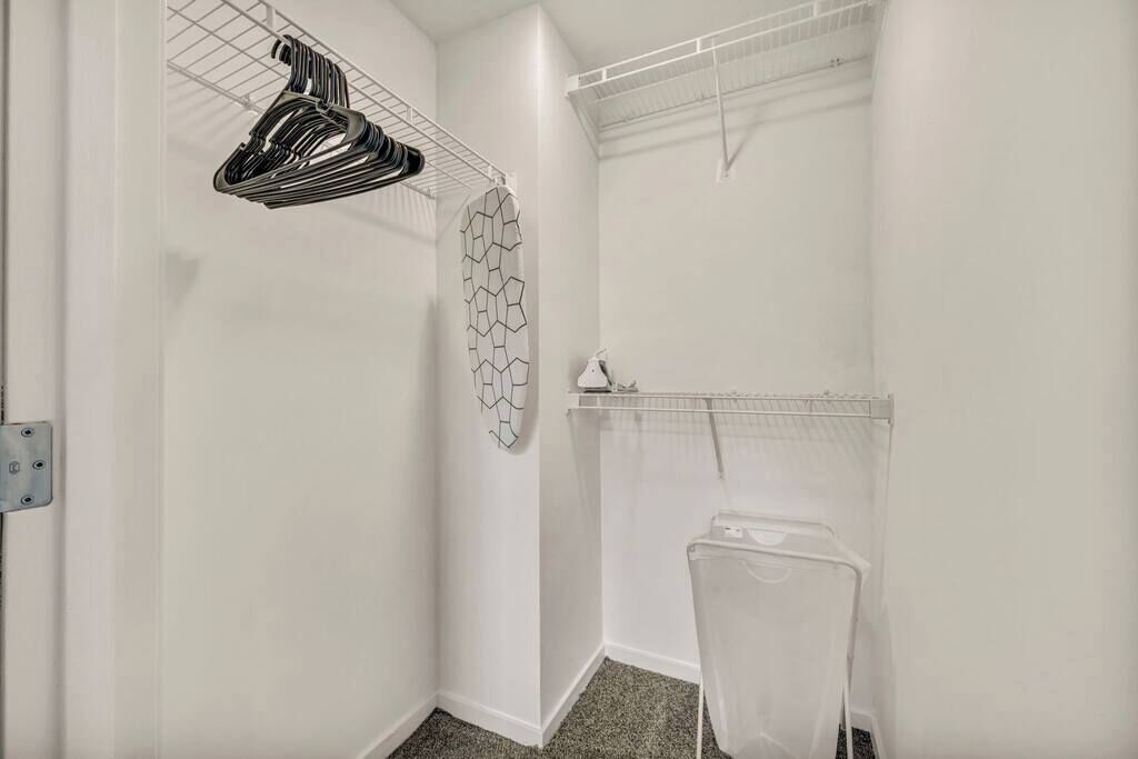 A small, white-walled room with a shower area, a towel rack, and a drying rack.