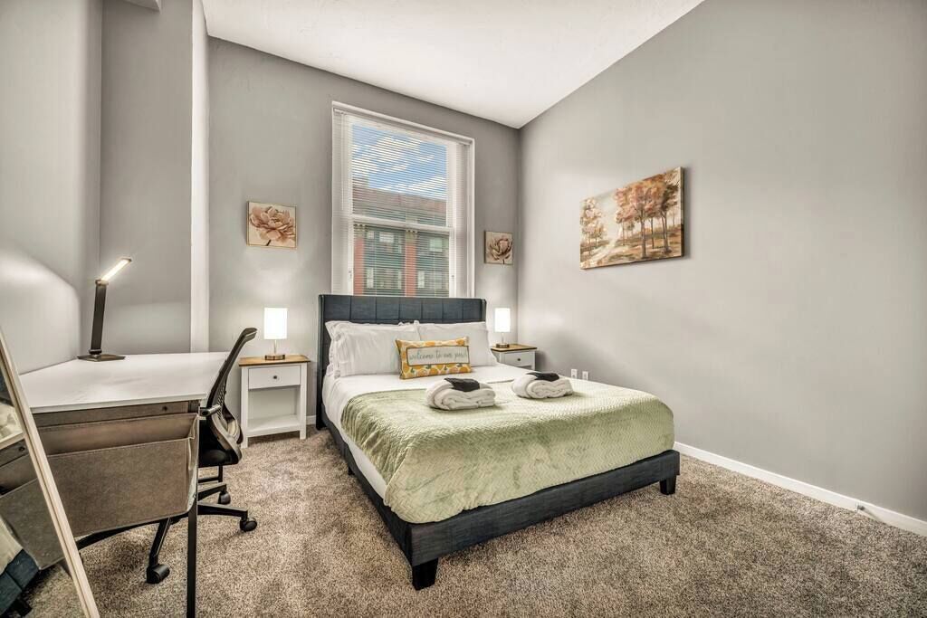 Une chambre à coucher avec un lit, un bureau, une chaise et des œuvres d’art accrochées aux murs.