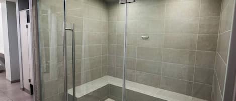Une douche fermée par des parois de verre, dotée d’un banc, de murs carrelés et d’une poignée en métal.