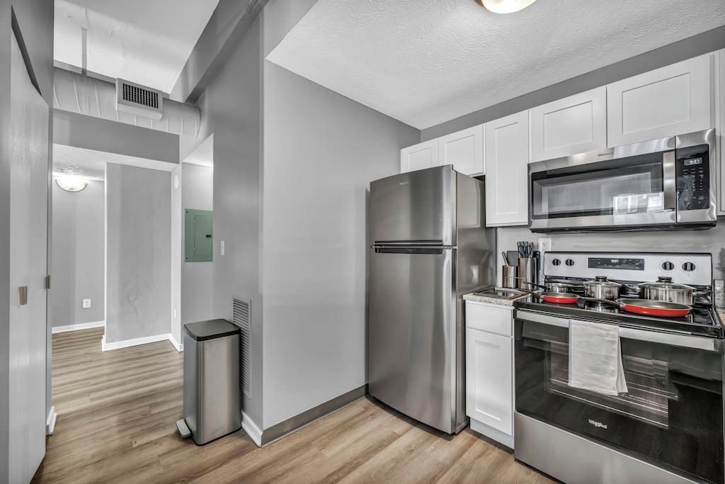 A modern kitchen with stainless steel appliances, white cabinetry, and a wooden floor.