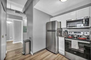 A modern kitchen with stainless steel appliances, white cabinetry, and a wooden floor. - Modern 1B in Heart of Downtown • Pool & Spa • Gym (Cleveland)