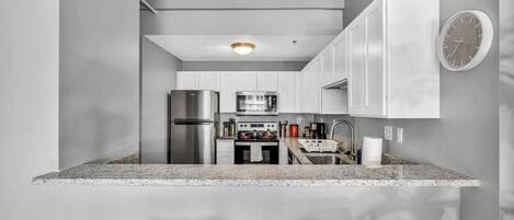 A modern kitchen with white cabinets, stainless steel appliances, and a granite countertop.
