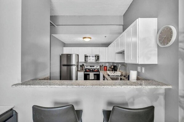 A modern kitchen with white cabinets, stainless steel appliances, and a granite countertop.