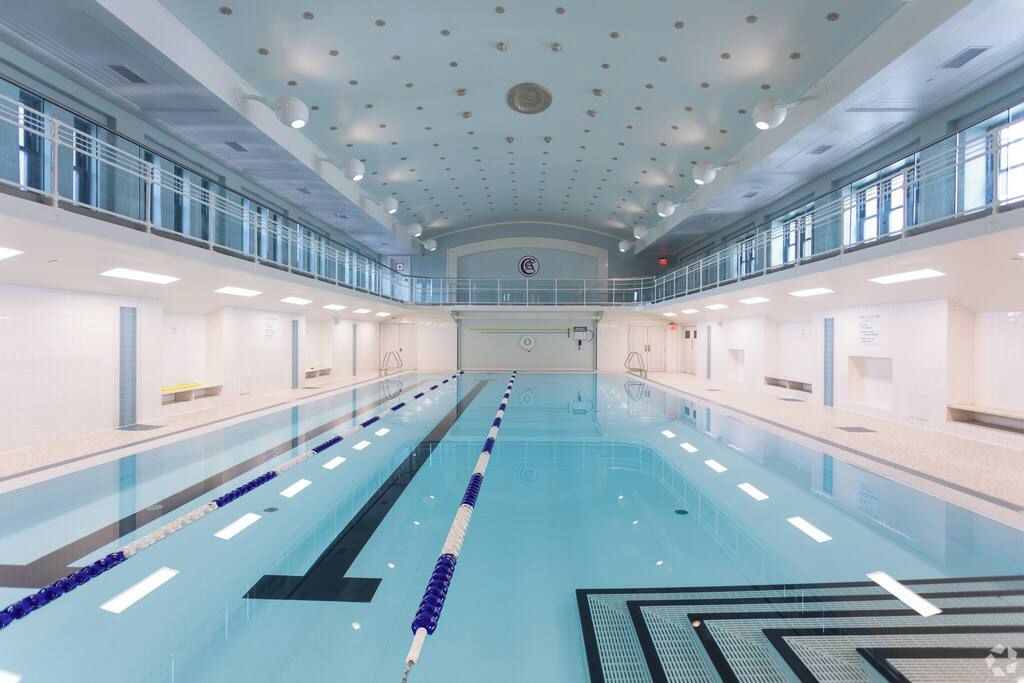 Una amplia piscina interior con carriles bien definidos, techo alto con luces distribuidas uniformemente y barandilla de vidrio en el nivel superior.