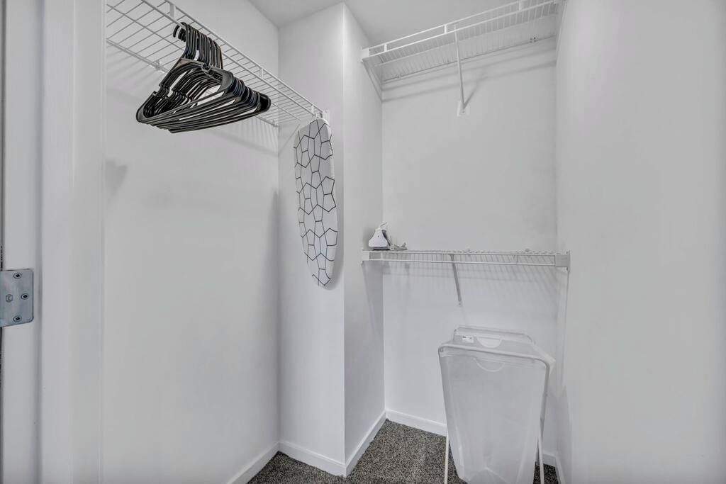 A small, white laundry room with a metal drying rack, a wall-mounted drying rack, and a plastic laundry basket.