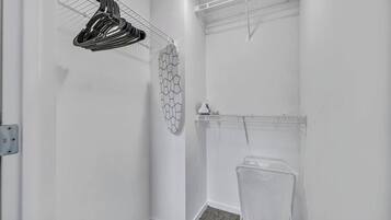 A small, white laundry room with a metal drying rack, a wall-mounted drying rack, and a plastic laundry basket.