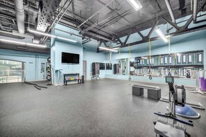 A spacious gym with exercise equipment, a large mirror, and a television on the wall. - HUGE Loft in Heart of Downtown • Pool/Sauna • Gym (Cleveland)