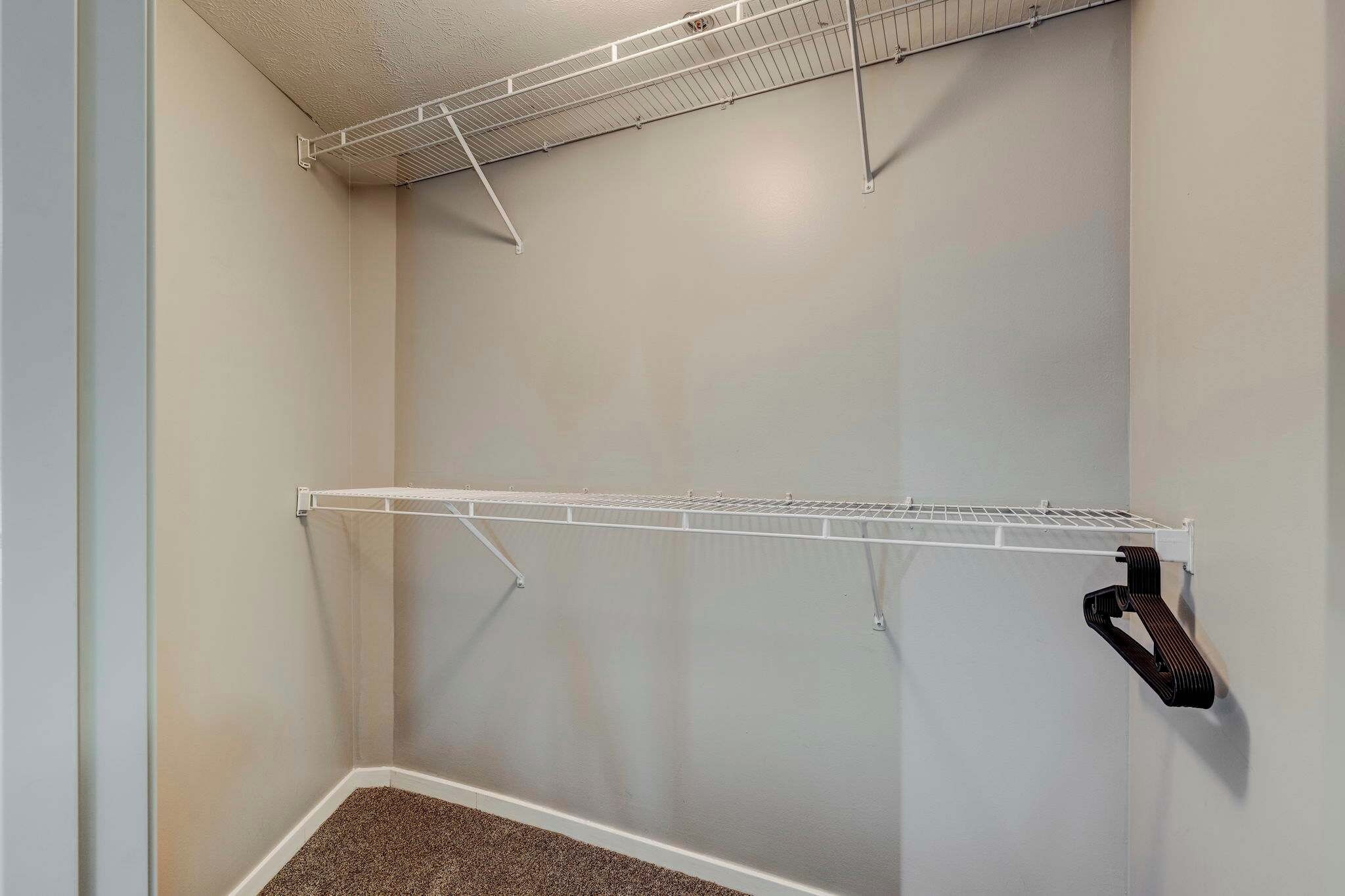 A closet with two white wire shelves and a black towel rack.