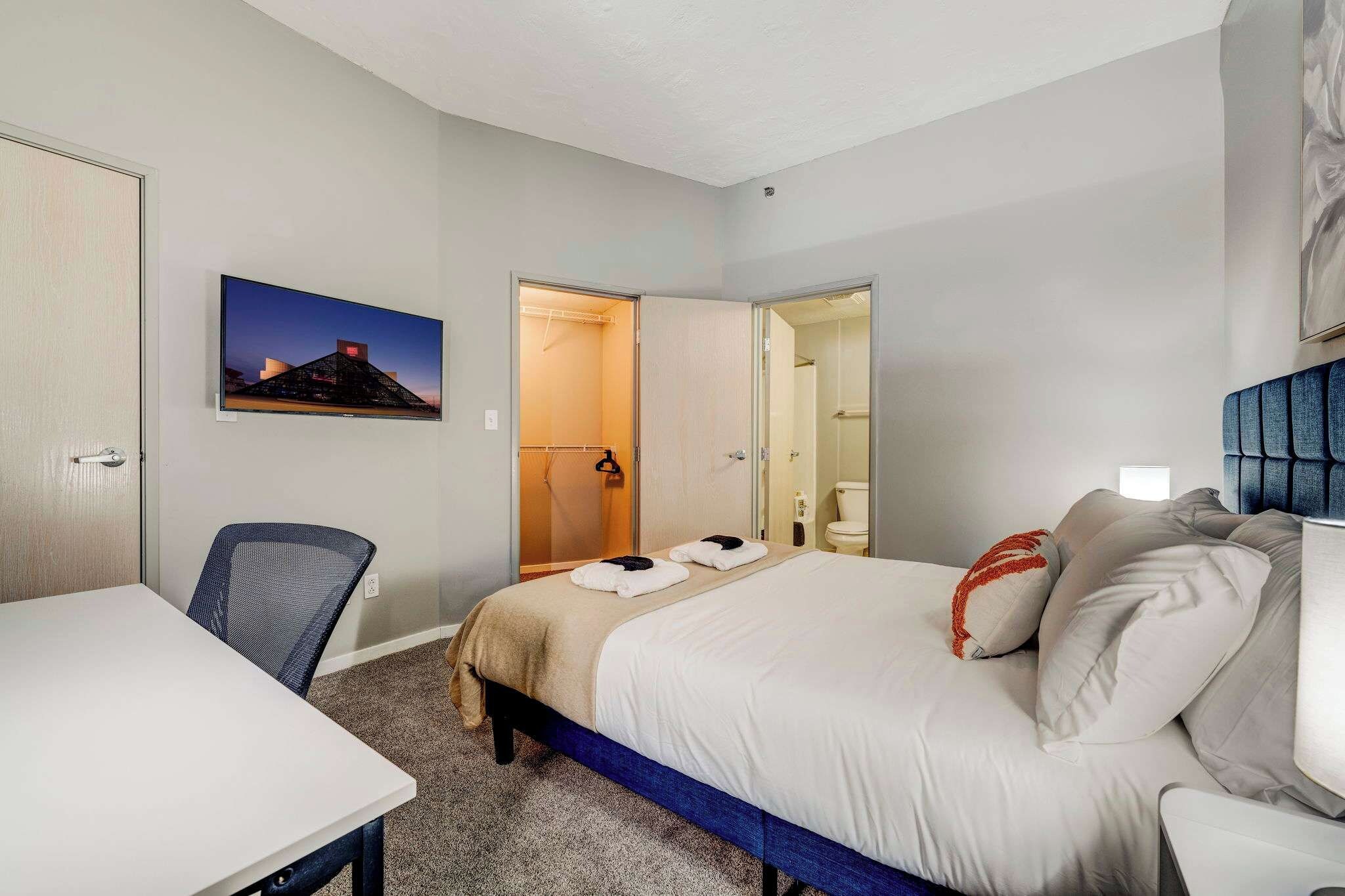 Ett hotellrum med en säng, ett skrivbord, en stol, en tv och ett badrum som syns genom en öppen dörr.