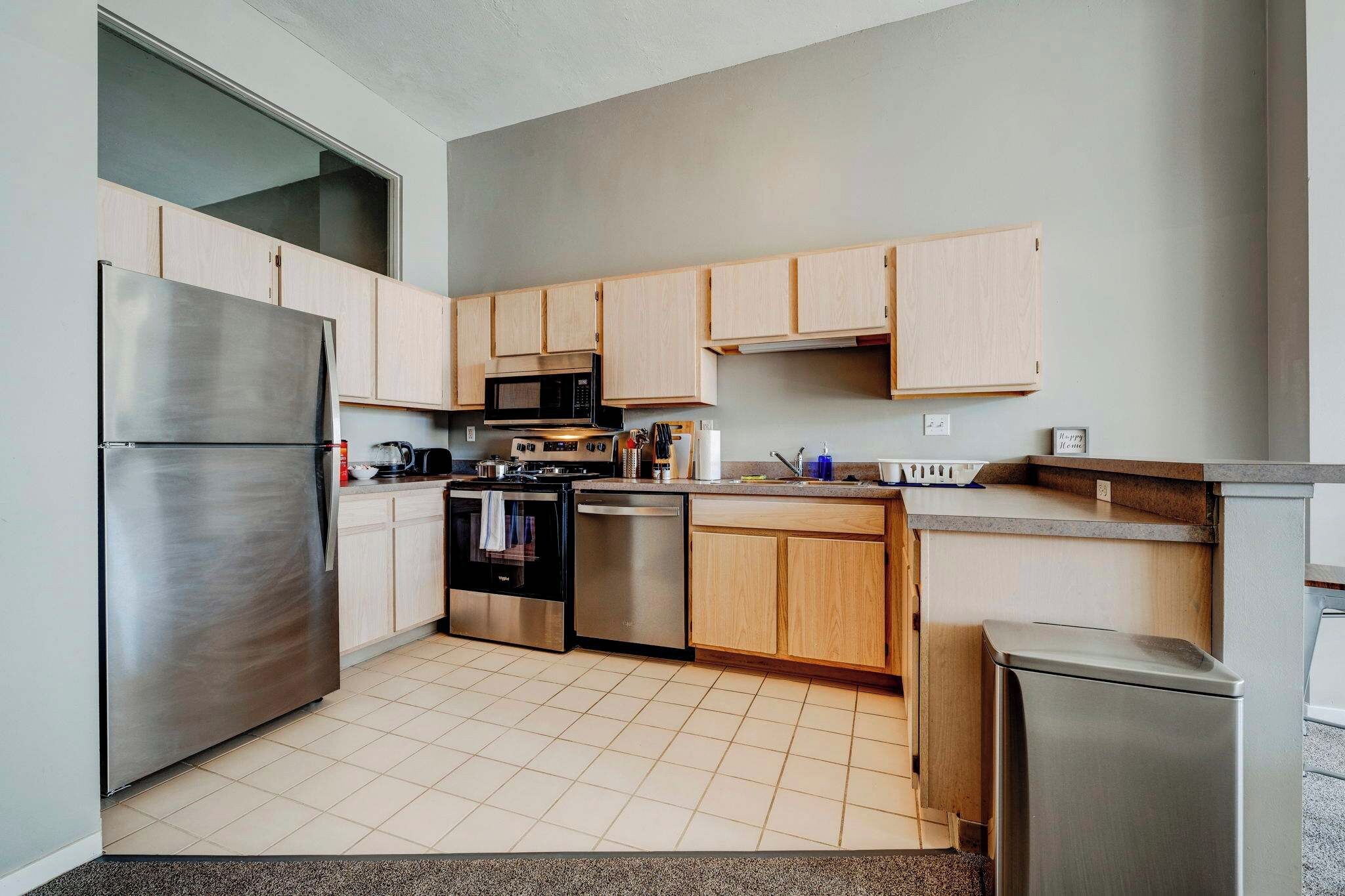 A modern kitchen with stainless steel appliances, wooden cabinets, and a tiled floor.