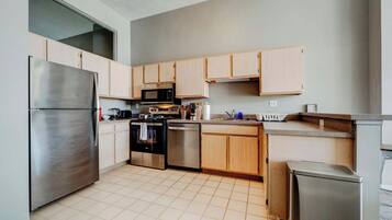A modern kitchen with stainless steel appliances, wooden cabinets, and a tiled floor.