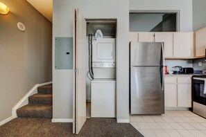 A compact kitchen with a built-in washer and dryer, a stainless steel refrigerator, and light wooden cabinets. - HUGE Loft in Heart of Downtown • Pool/Sauna • Gym (Cleveland)