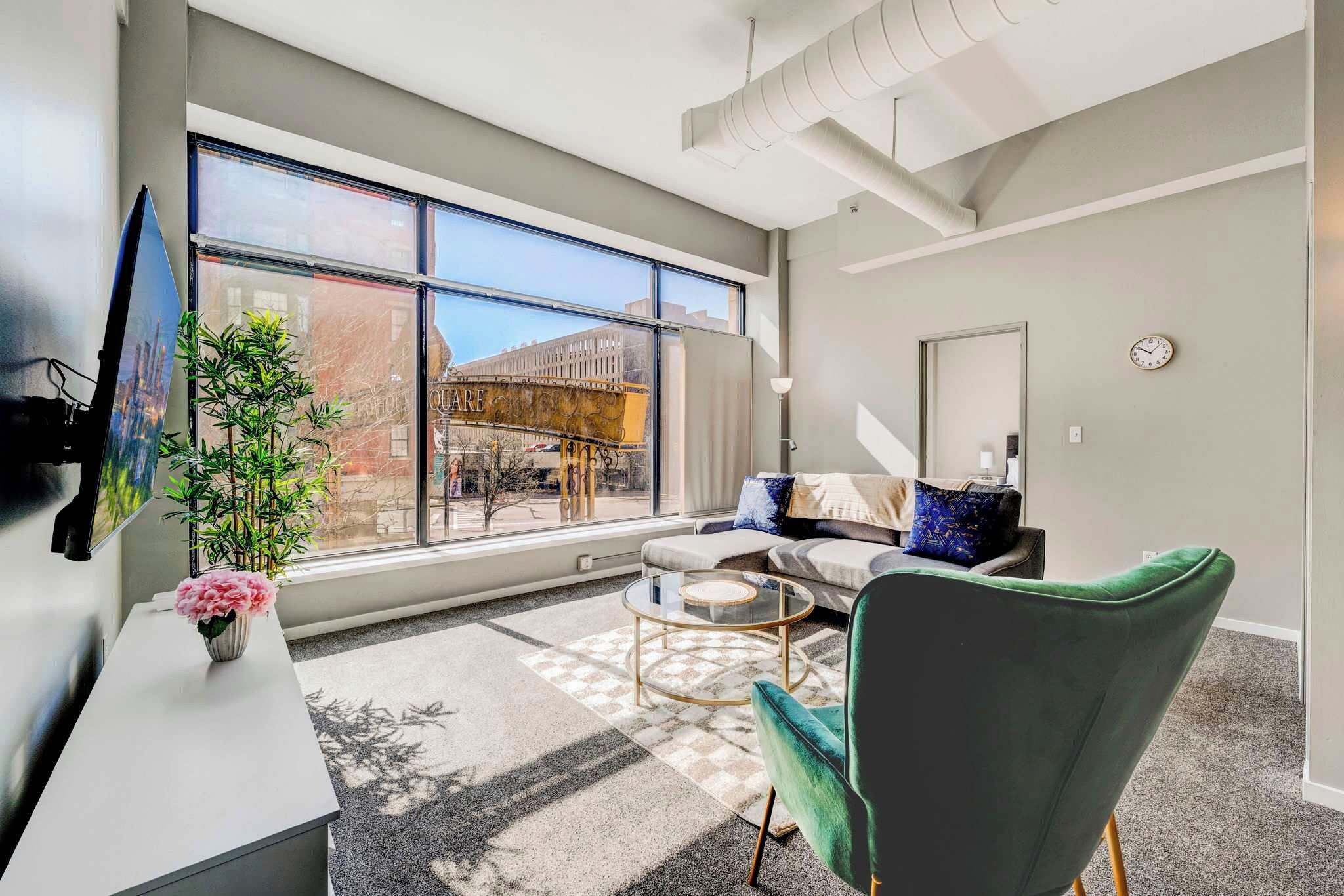 Una sala de estar moderna con un ventanal grande, un sofá, un sillón verde y una pequeña mesa de centro.